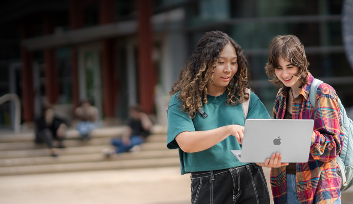 캠퍼스에 서서 MacBook 화면을 보고 있는 대학생 두 명